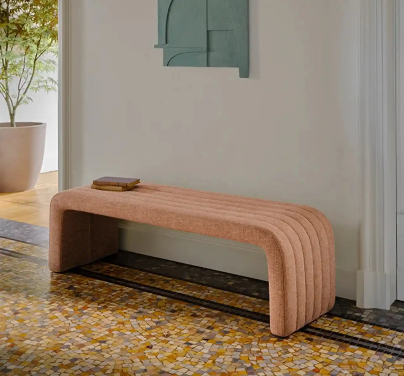 Banc design en tissu rose avec livres posés, sol en mosaïque et tableau abstrait dans un intérieur contemporain