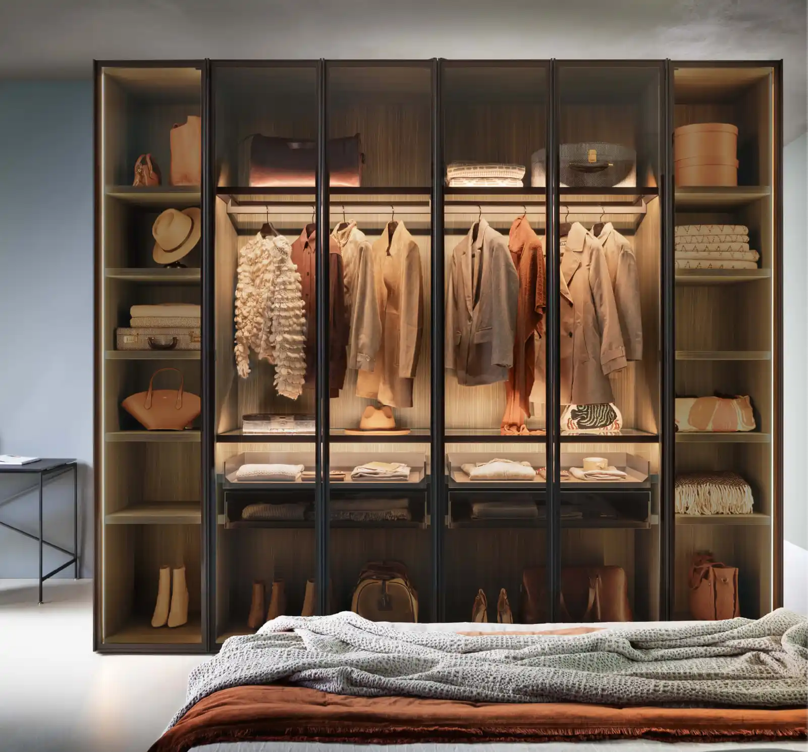 Armoire vitrée avec éclairage intégré, vêtements suspendus et rangements organisés dans une chambre moderne